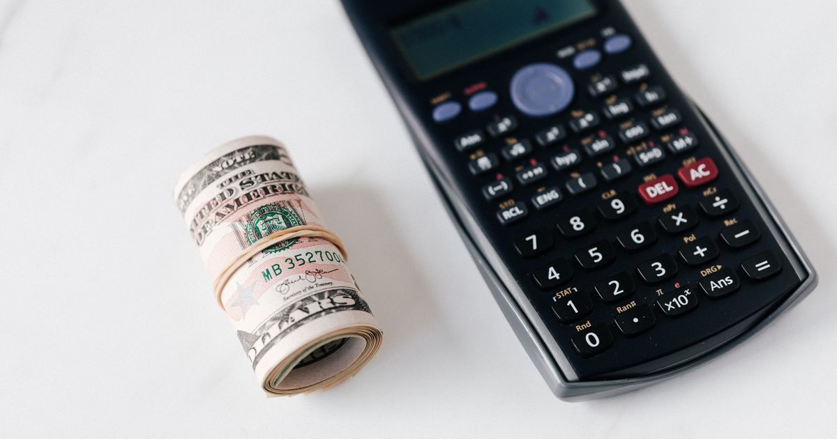 From above of modern electronic calculator with small display and buttons of different colors near roll of dollar bills on marble surface