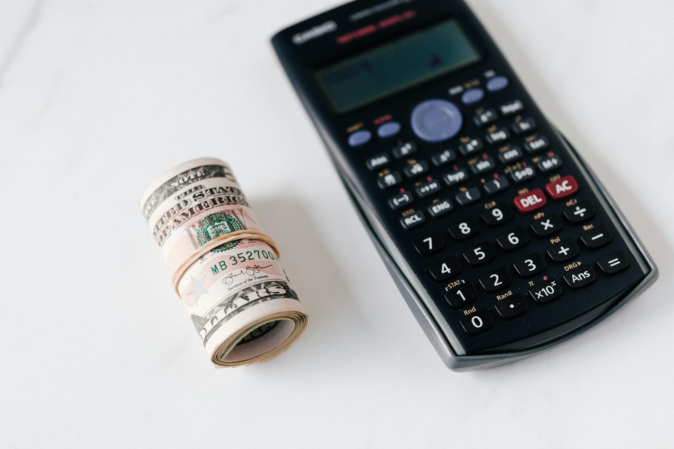 A calculator with multicolored buttons and a roll of greenbacks on the table