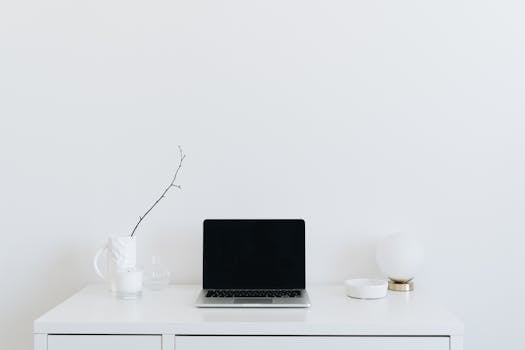 Simple and elegant white desk with a laptop, vase, and decor, ideal for a modern workspace.