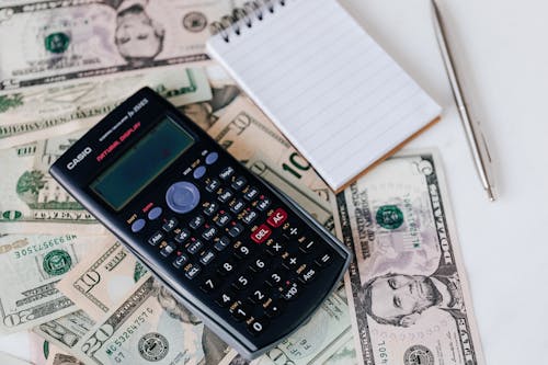 electronic calculator and notepad placed over United States dollar bills together with metallic pen for budget planning and calculation Stock Photo