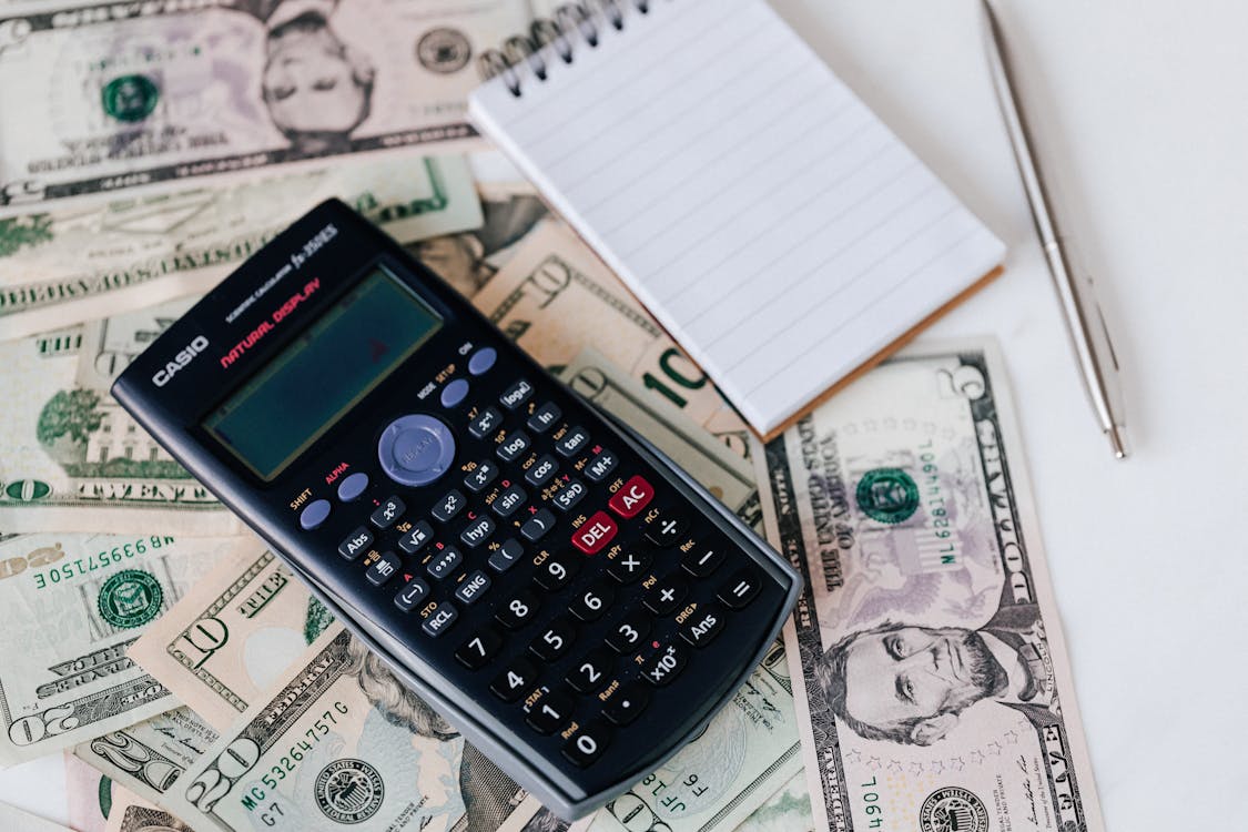 Free From Above Electronic Calculator And Notepad Placed Over United States Dollar Bills Together With Metallic Pen For Budget Planning And Calculation Stock Photo