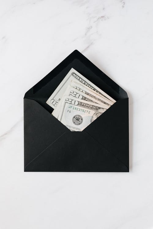 Top view of opened envelope with USA banknotes of 20 dollars placed on white marble desk illustrating concept of money gift or charity