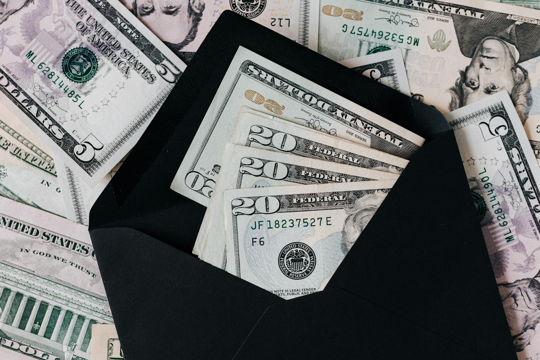 From above of dollar bills in opened black envelope placed on stack of United States cash money