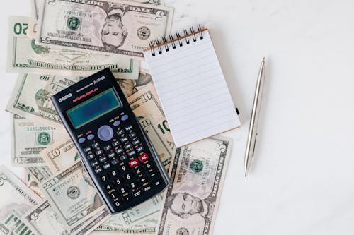 Calculator and notepad placed over stack of USA dollars