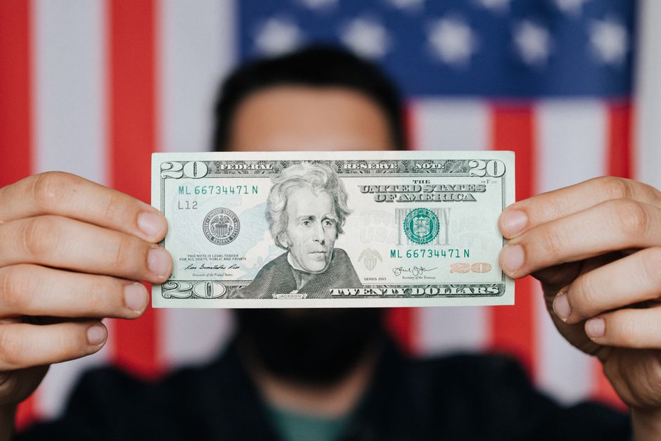 Blurred adult man demonstrating United States paper bill for personal financial operations hiding face on background of USA national flag