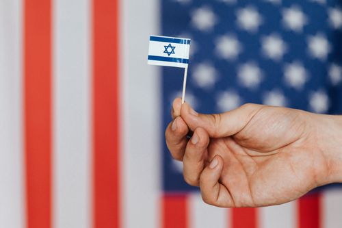 Free Closeup of crop unrecognizable person holding small flag of Israel before huge flag of United States of America on background Stock Photo
