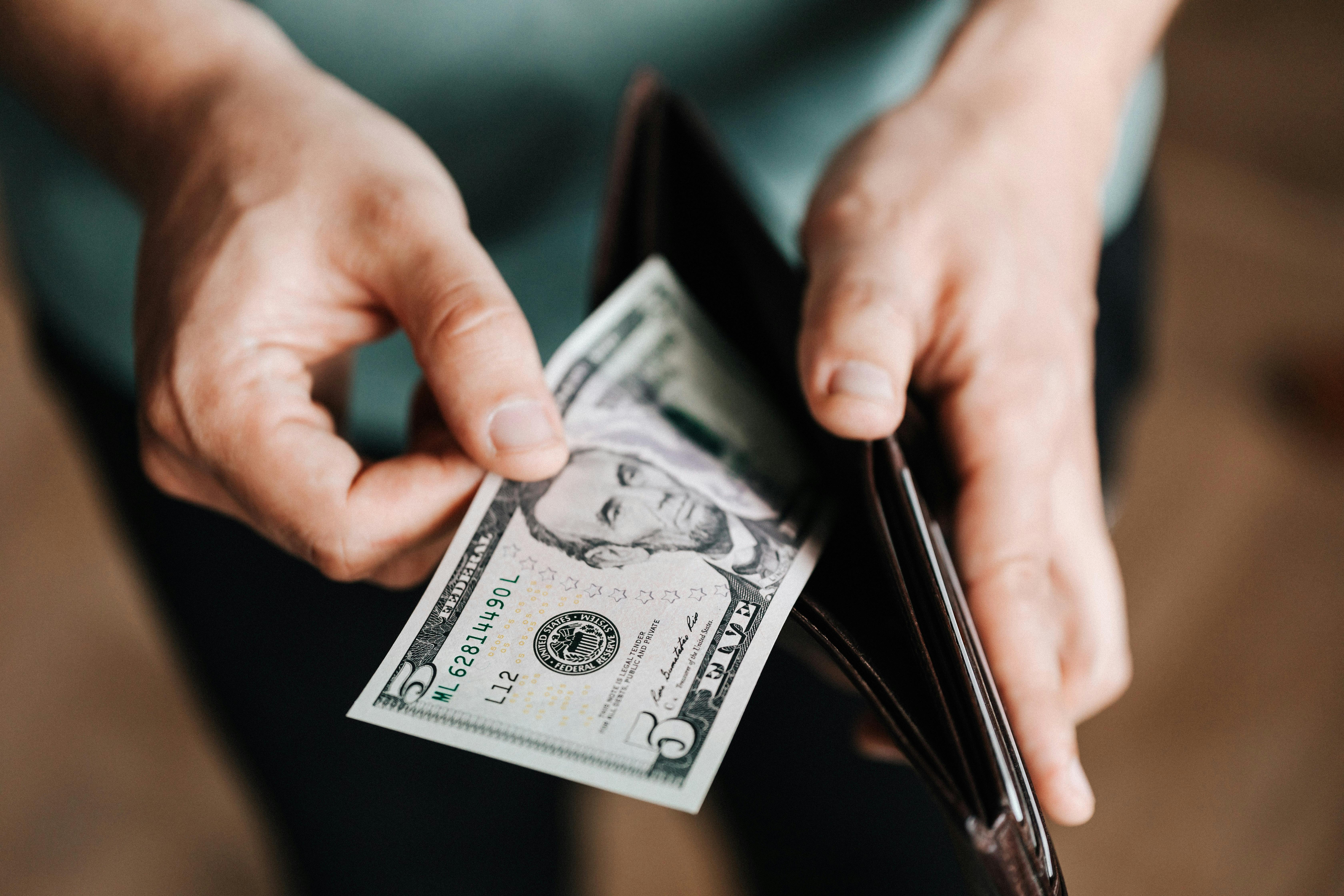 Man pulling $5 bill ourt of wallet.