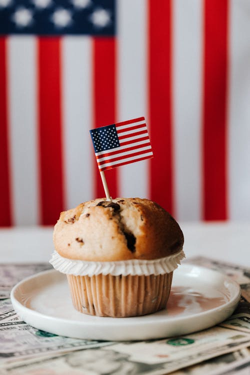 Free Appetizing cake decorated small colorful flag on white plate placed on paper dollars of USA before official flag of American on background Stock Photo
