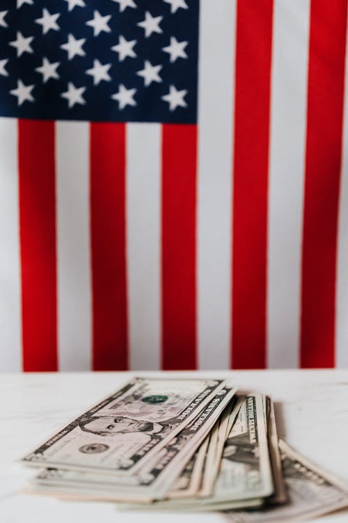 Closeup of dollars pile placed on white surface of table against flag of United States of America