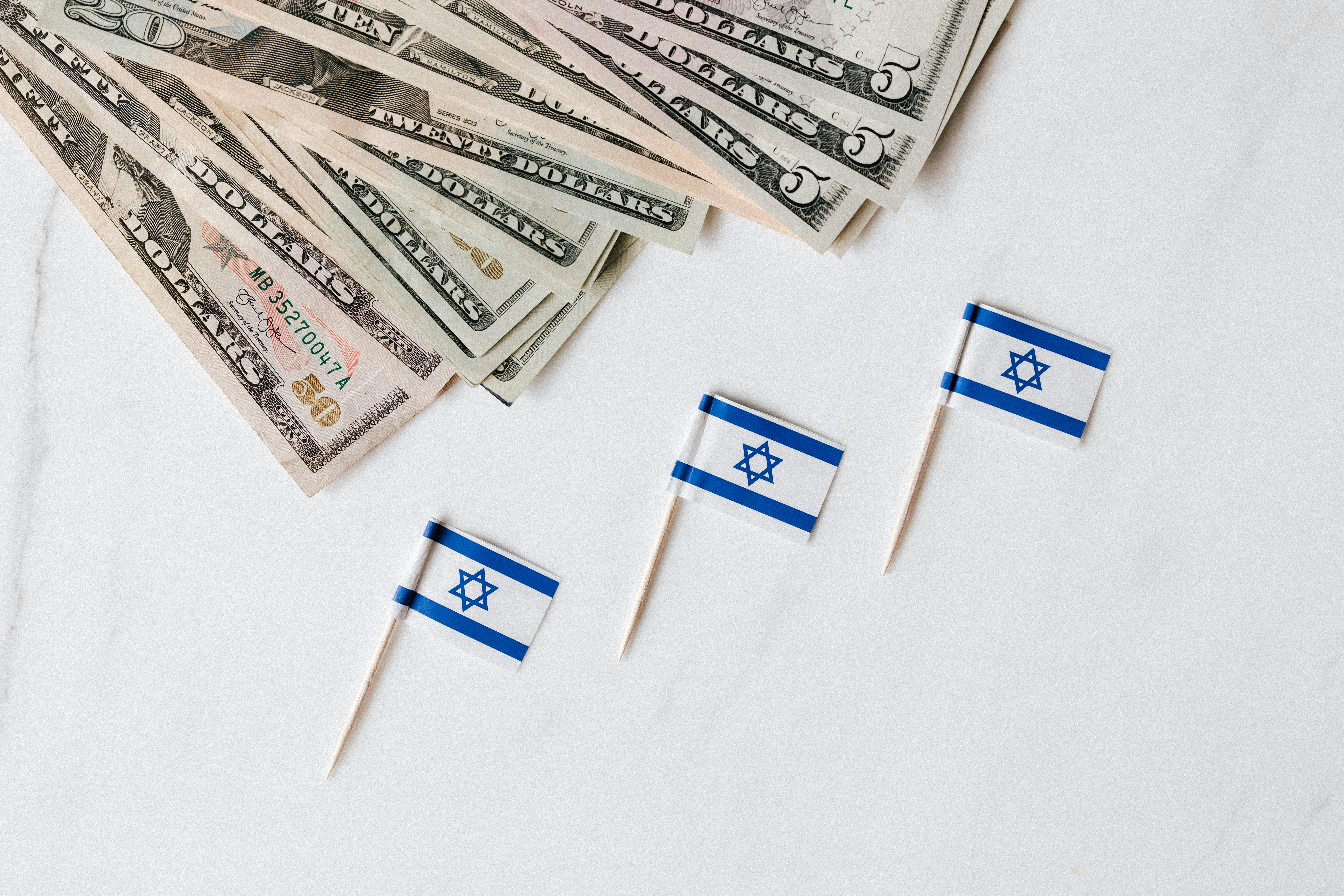 set of israeli flags on toothpick and heap of dollars