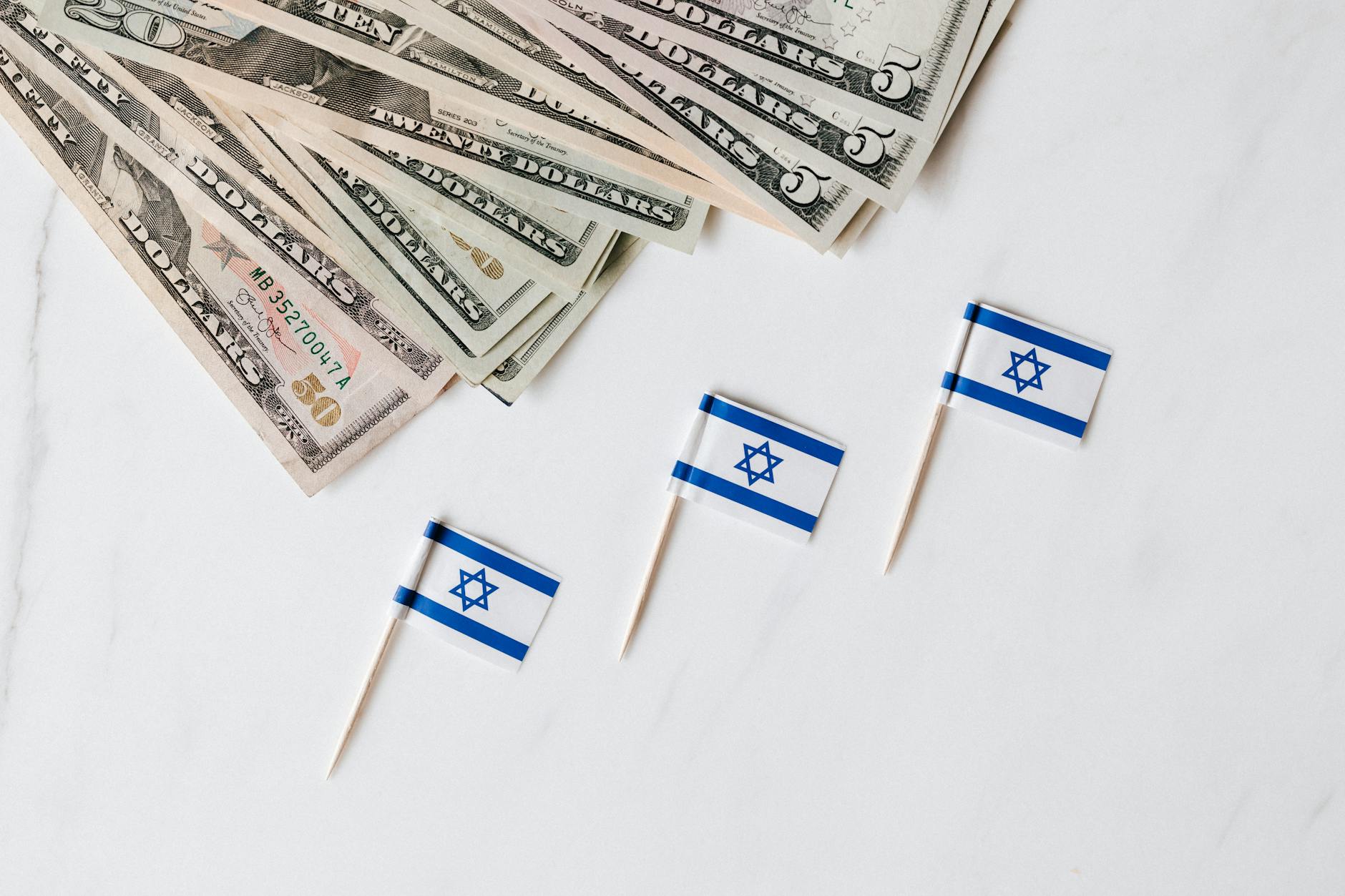 Top view of bundle of different nominal pars dollars and Israeli flags on toothpicks placed on white surface of marble table