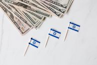 Top view of bundle of different nominal pars dollars and Israeli flags on toothpicks placed on white surface of marble table