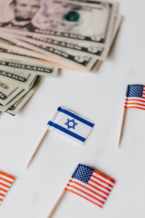 From above set of miniature toothpick flags of USA and Israel placed on white table with dollar banknotes