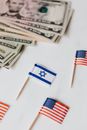 From above set of miniature toothpick flags of USA and Israel placed on white table with dollar banknotes