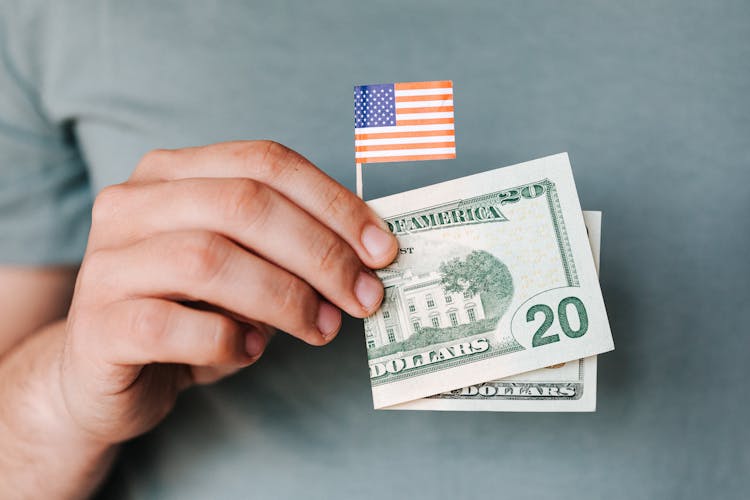 Crop Person Showing Twenty Dollar Bill And Miniature USA Flag