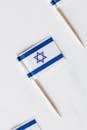 Top view collection of small paper flags of Israel on toothpicks placed in line on white surface