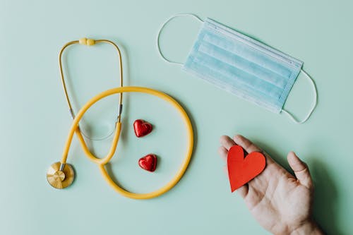 Free Top view of crop anonymous person hand with red paper heart on table with stethoscope and …