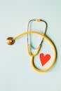 Medical stethoscope with red paper heart on white surface