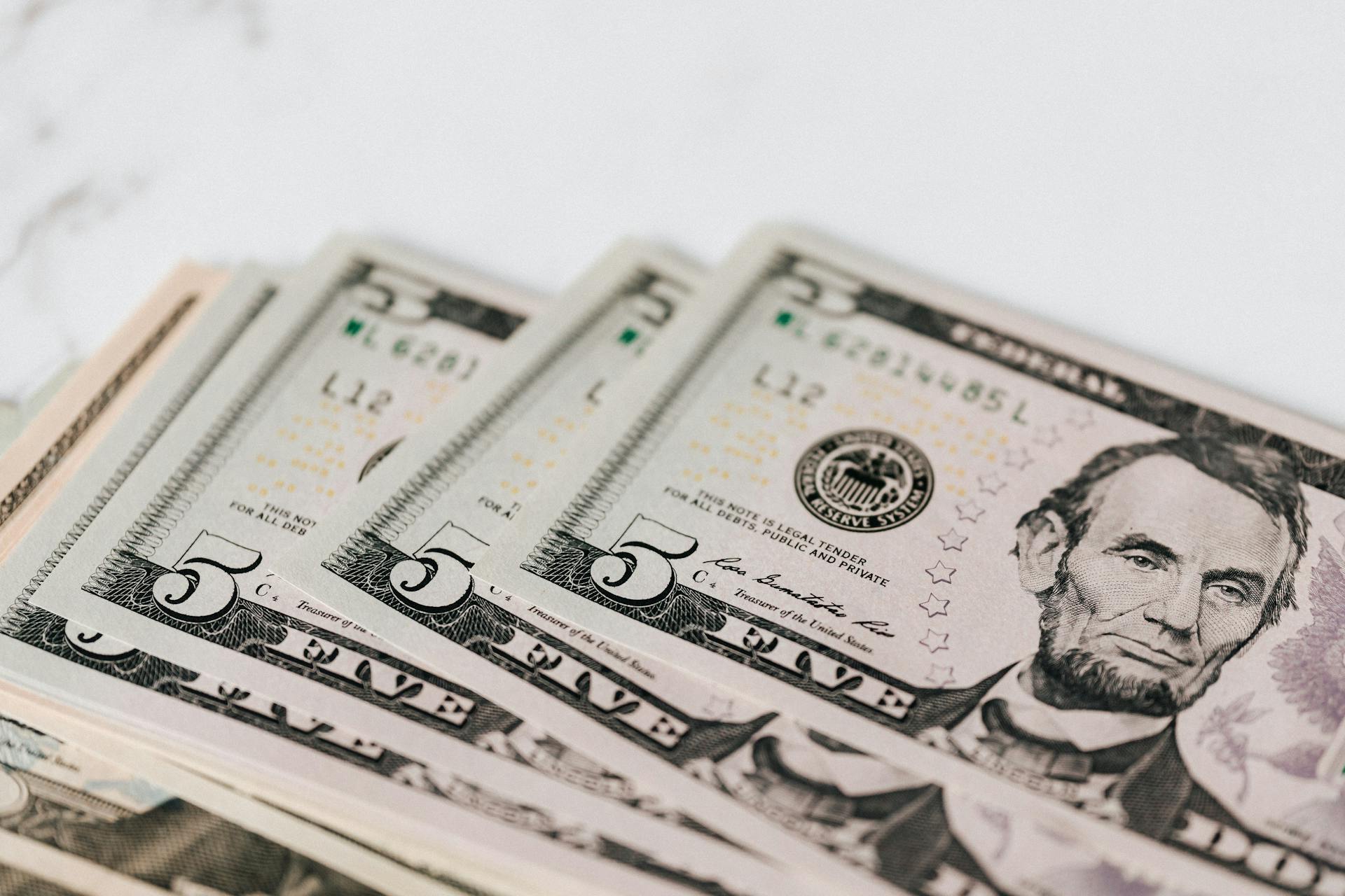 From above of pile of five dollar bills placed on white marble surface