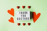 Top view of red heart shaped decorative elements and white retro light box with THANK YOU DOCTORS gratitude message arranged on green background