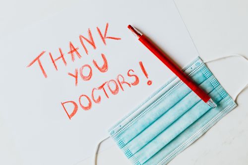 Free Red handwritten thank you note with a face mask and pen, showing appreciation for doctors. Stock Photo