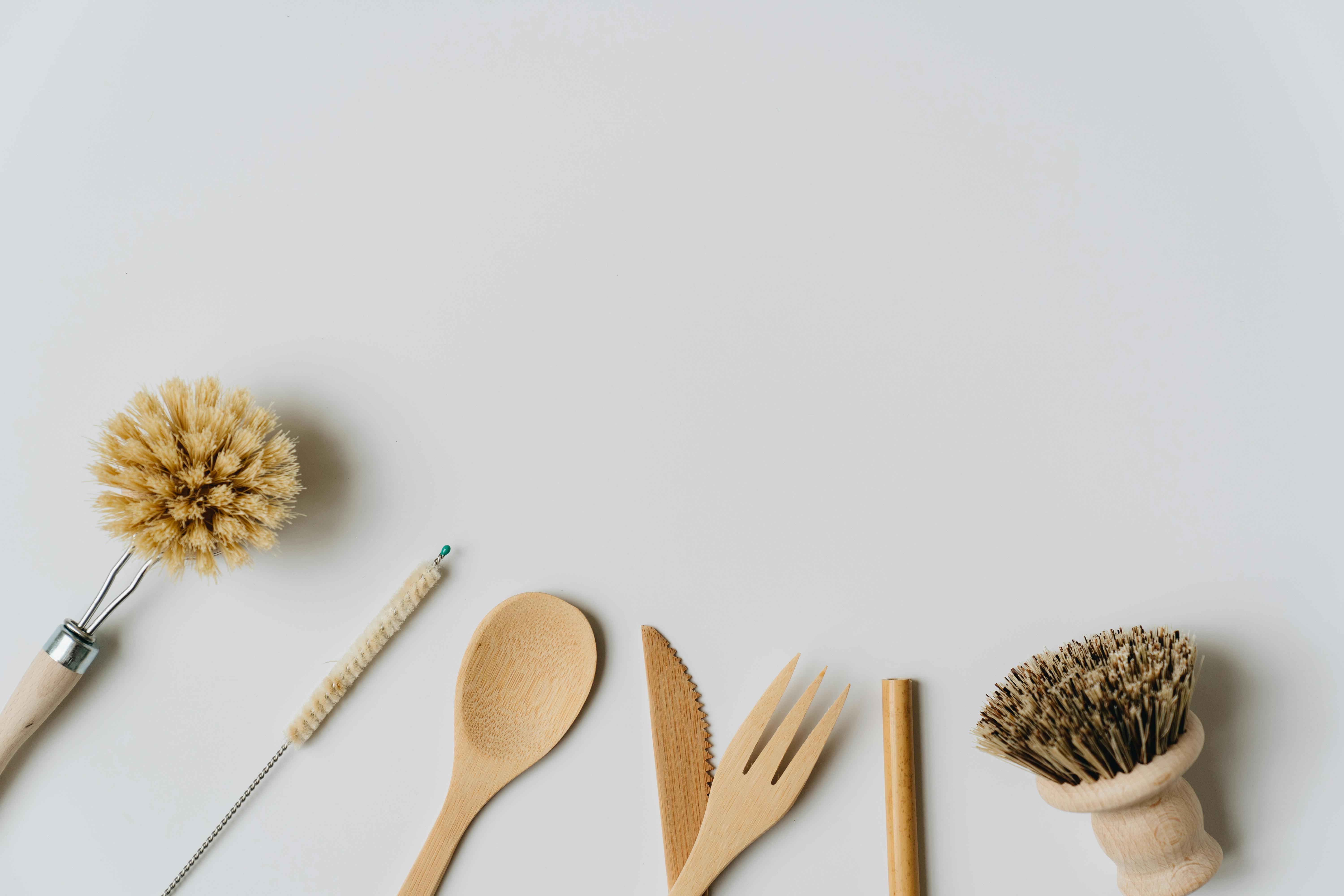 Sustainable wooden kitchen utensils and brushes on a white background, promoting eco-friendly living.