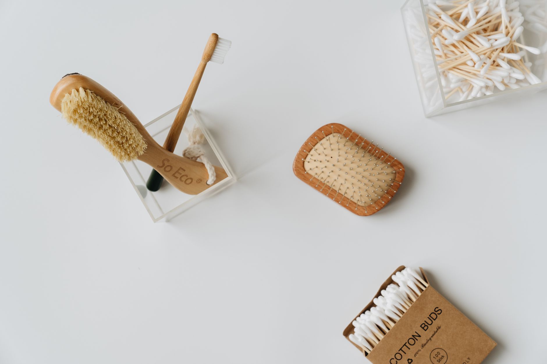 A top view of eco-friendly hygiene products, including bamboo brushes and cotton buds on a white desk.