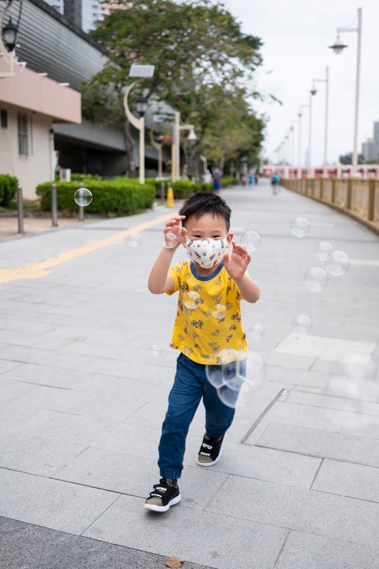 A Boy In A Yellow Shirt Chasing Bubbles