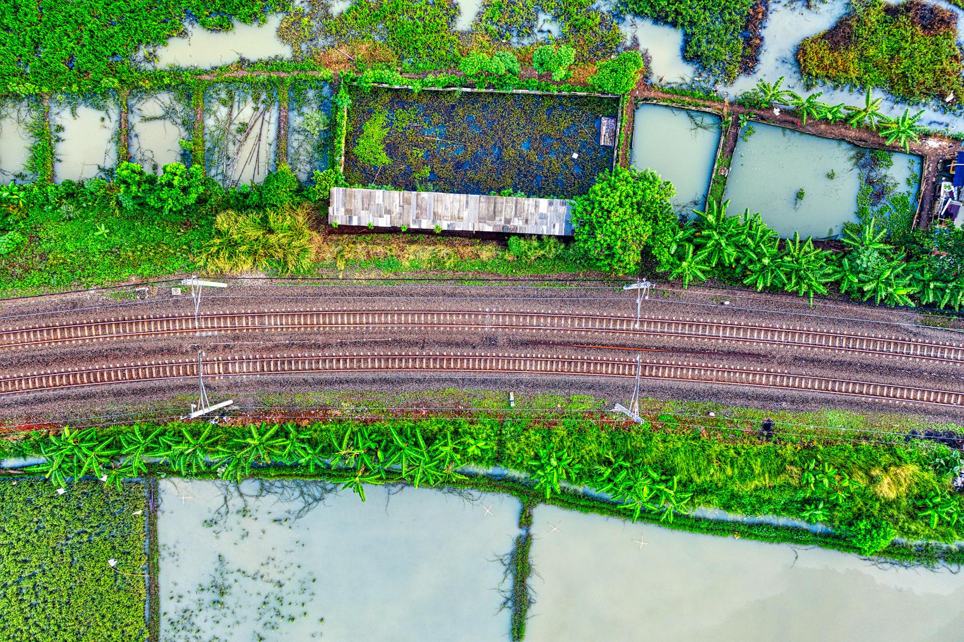 Aerial shot of railway tracks crossing vibrant agricultural fields and water bodies in Banten, Indonesia.