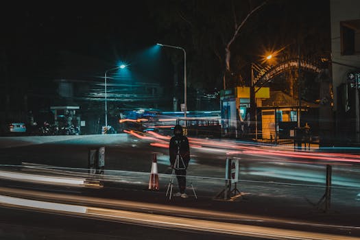 Night street scene capturing motion with vibrant light trails and a standing person.