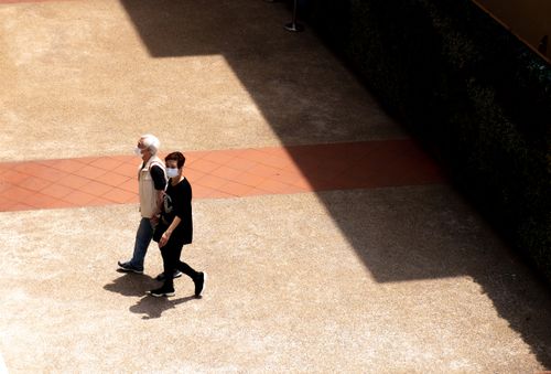 Free Aerial shot of a couple walking outdoors with face masks in Hong Kong, casting shadows on a sunny day. Stock Photo