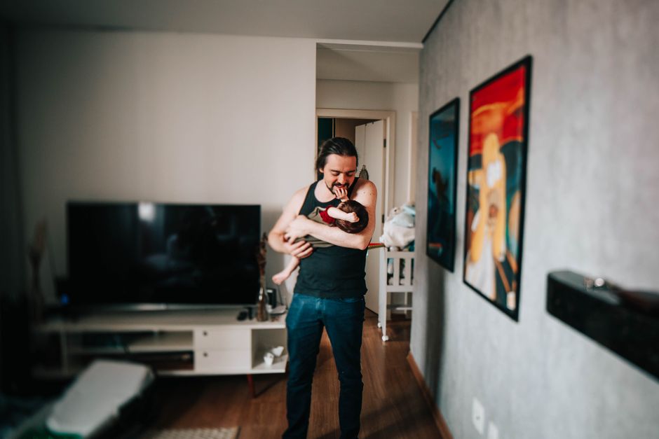 Cheerful ethnic man cuddling gently little child while spending time together and playing in flat