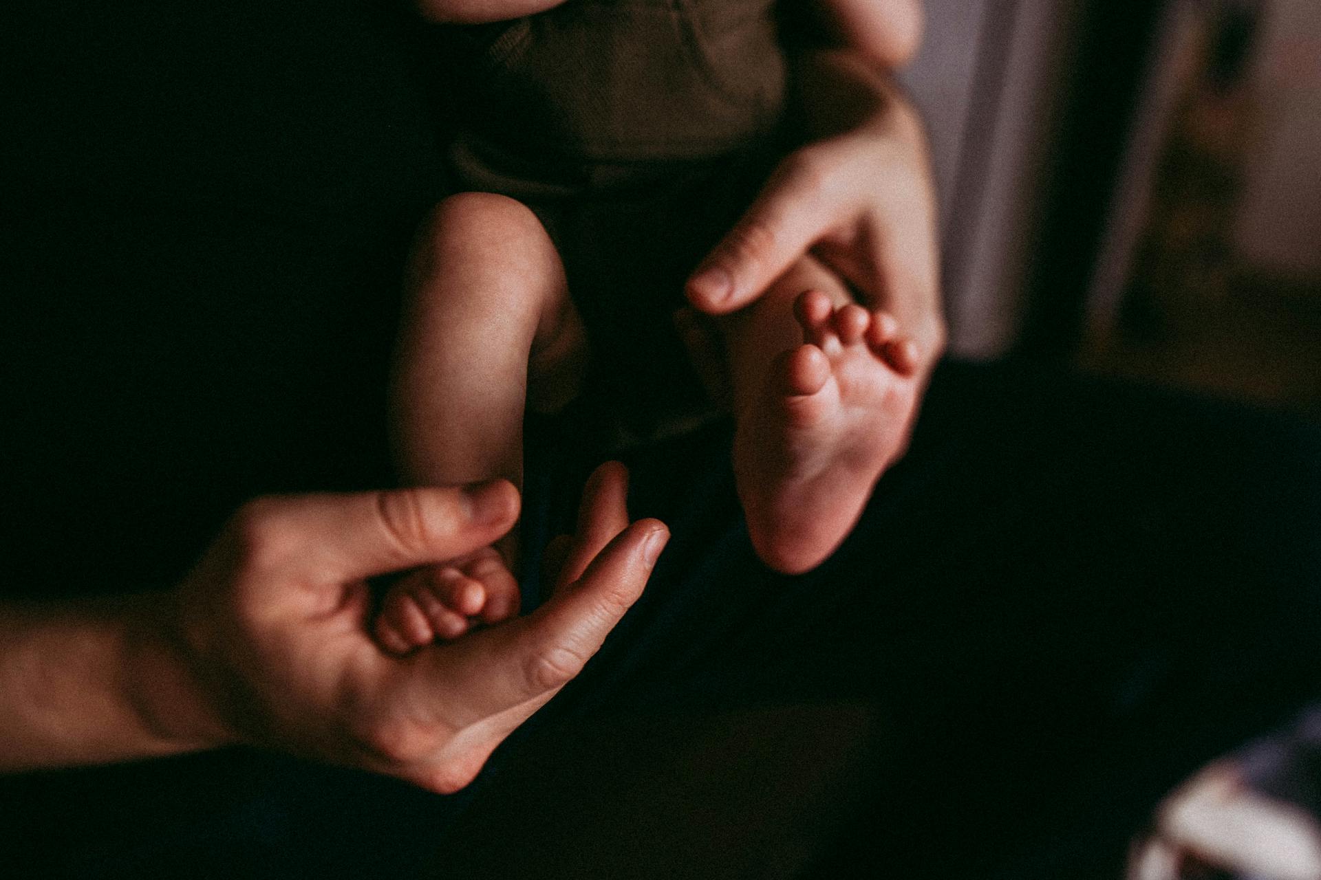 A tender moment captured as a parent gently holds a baby's feet in a serene indoor setting.