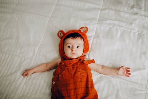 Adorable baby in red wear lying on bed at home