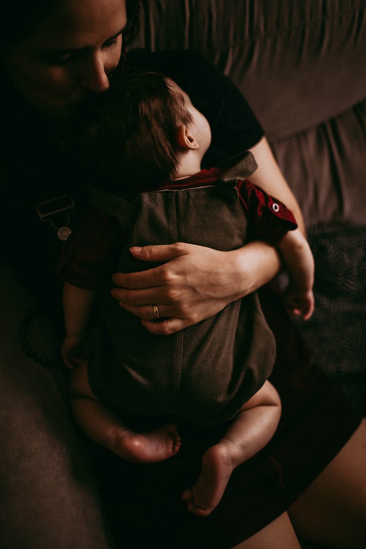 Crop Woman Embracing Sleeping Child On Sofa