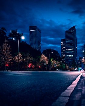 A vibrant nighttime view of Warsaw's skyline with illuminated buildings and a quiet street.