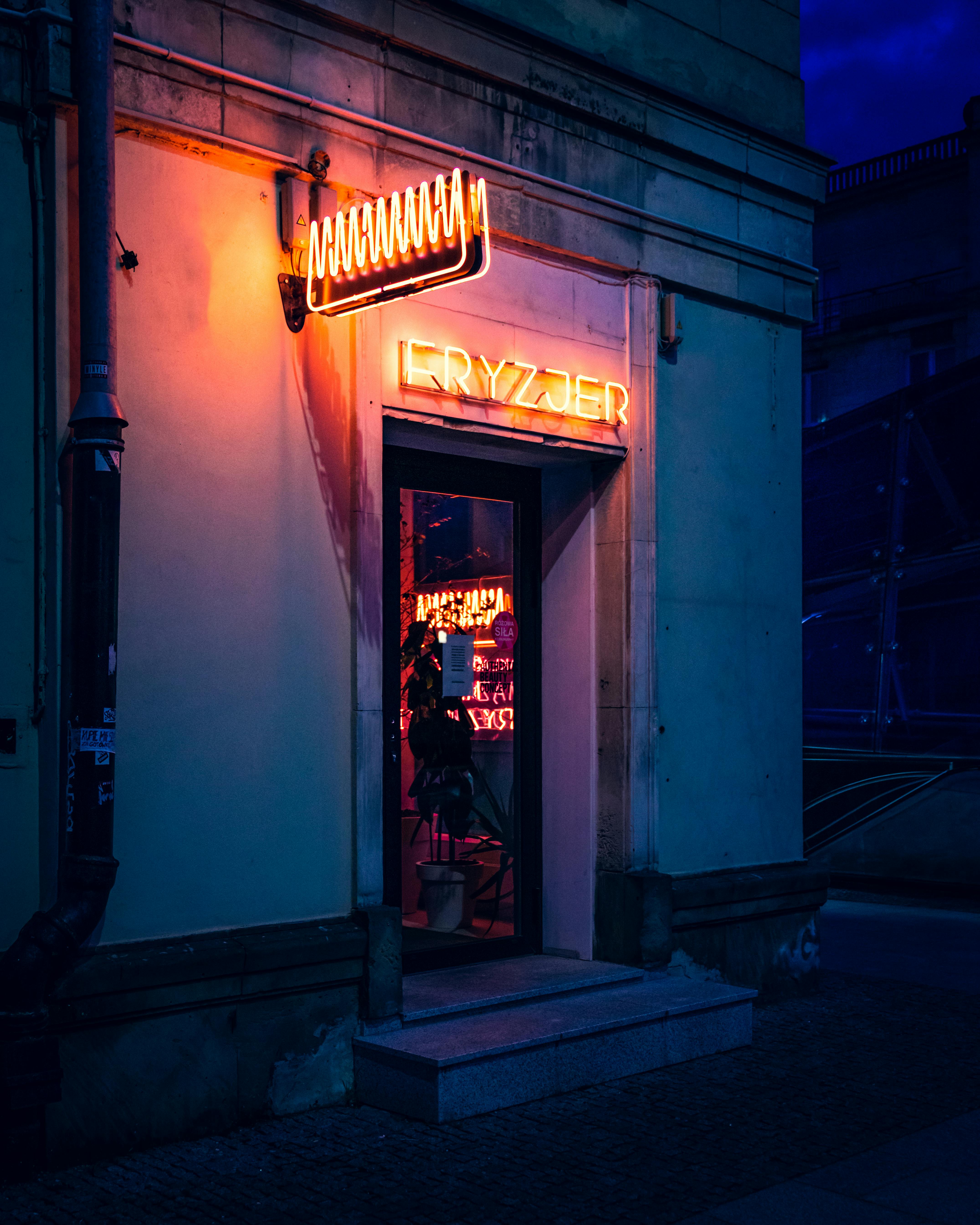 Vibrant neon sign adorns a barbershop entrance in Warsaw, Poland at night.