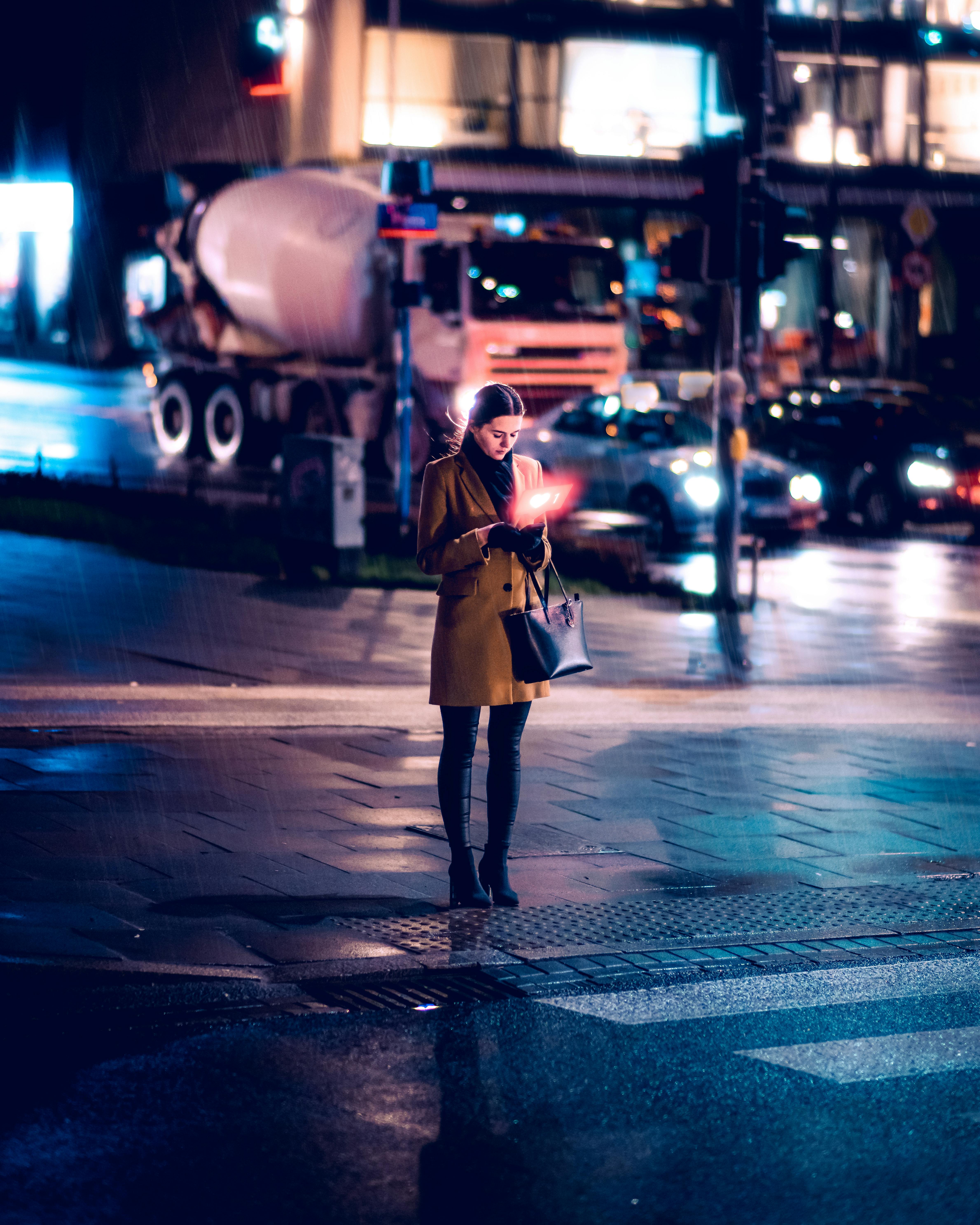 Caucasian woman using a smartphone on a rainy night street in Warsaw, Poland.