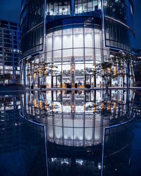A stunning reflection of a modern skyscraper in Warsaw with neon lights at night.