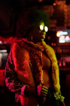 Portrait of a fashionable woman wearing sunglasses and fur coat in a vibrant nightclub setting.