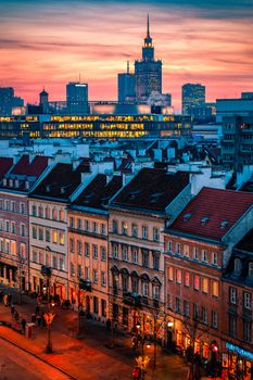 A vibrant sunset casts warm hues over Warsaw's cityscape, highlighting historic and modern architecture.