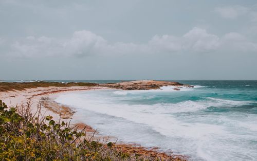 Free From above spectacular view of wavy sea with foam near sandy beach with growing grass under cloudy sky in stormy weather Stock Photo