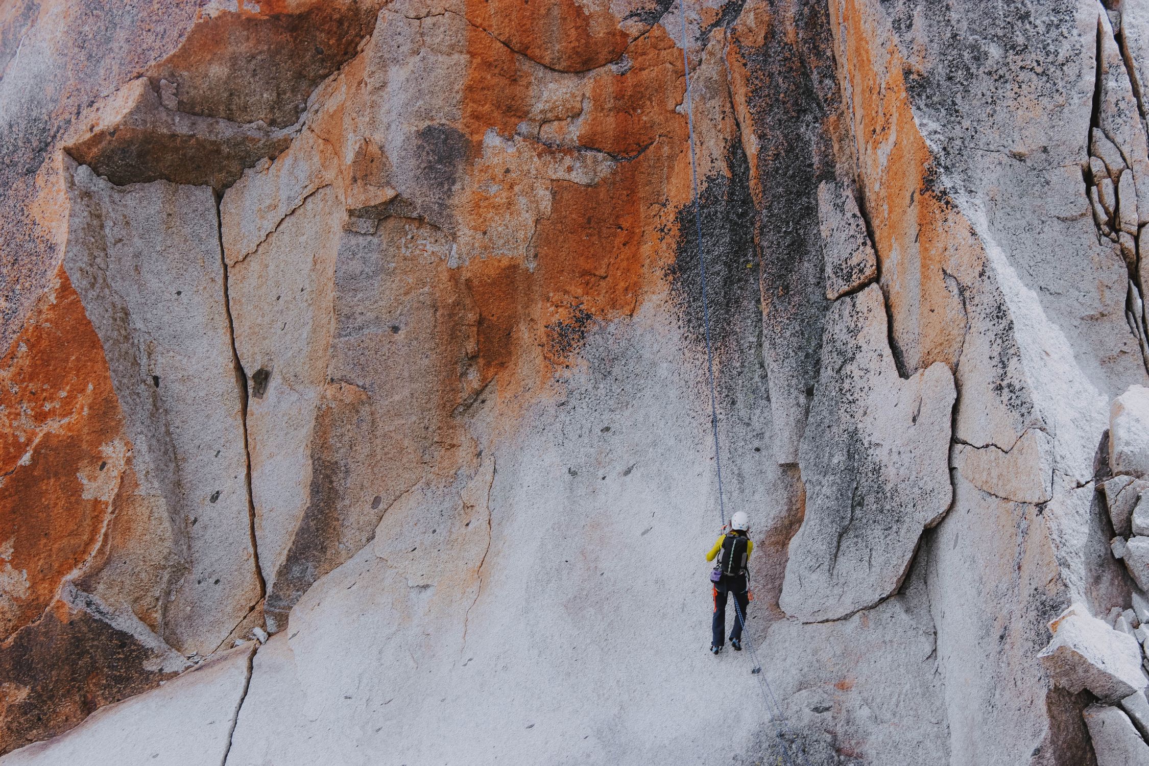 Alpine climber ascending weathered mountain rock face in daylight