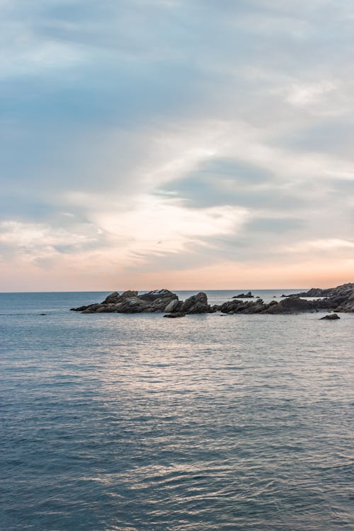 Spectacular view of rippled ocean with rough rocky formations under cloudy shining sky at sundown