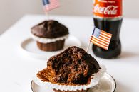 Sweet cakes with toothpick american flags placed on table with soda bottle