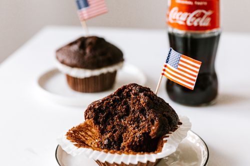 Free Delicious bitten chocolate cupcakes decorated with cocktail flag of USA and served on white table with bottle of coke Stock Photo