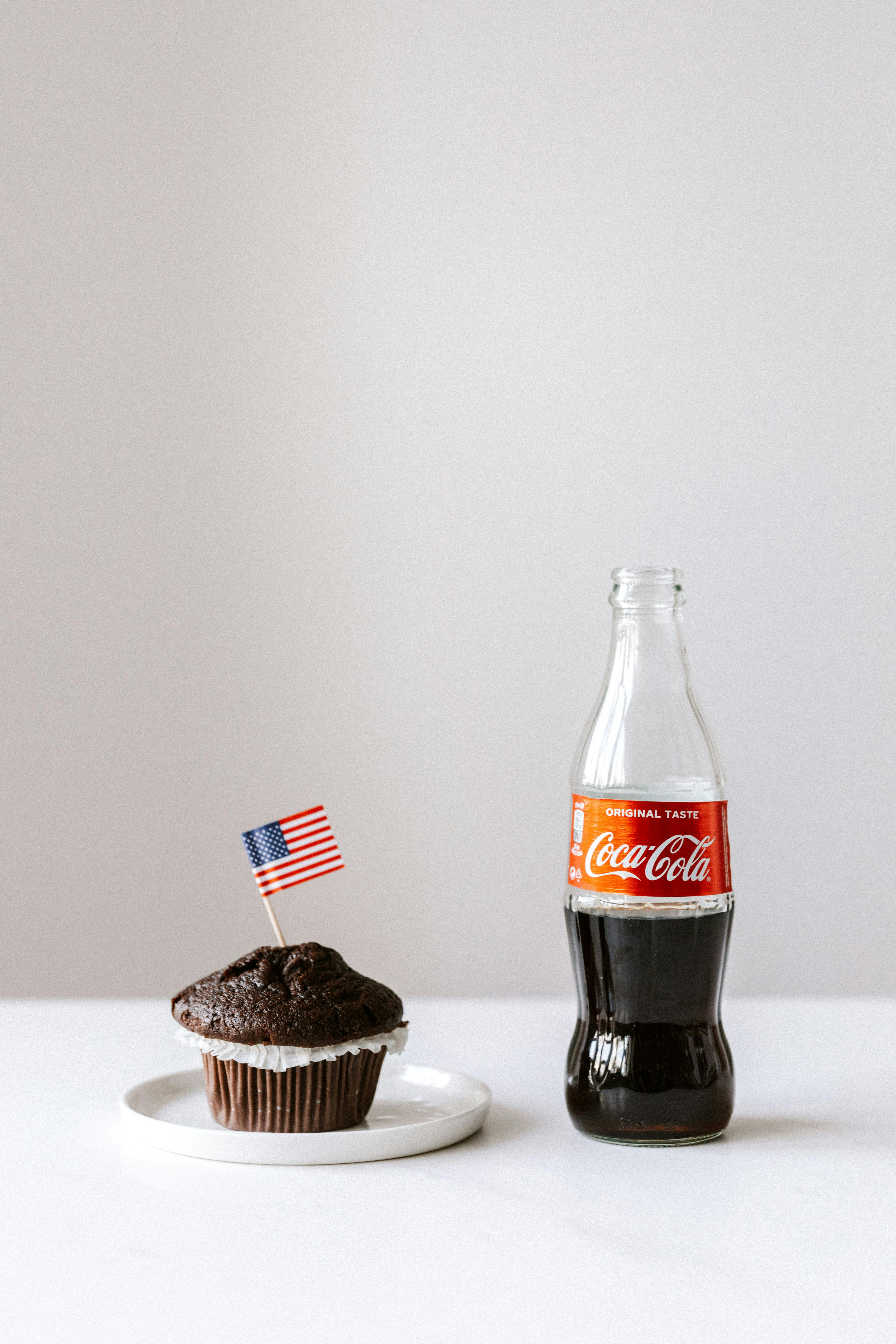 muffin with miniature us flag and coke bottle placed on white table