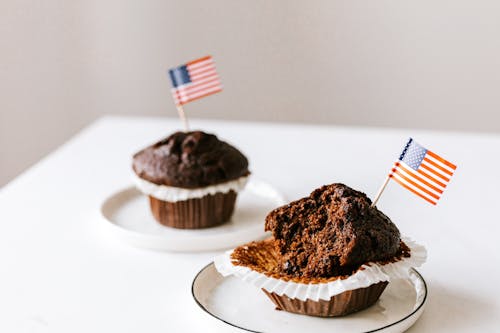 Free From above of bitten and whole festive chocolate cupcakes decorated with miniature american flags and placed on white table Stock Photo