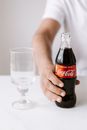 Crop anonymous male in white t shirt sitting at table with bottle of coke and glass