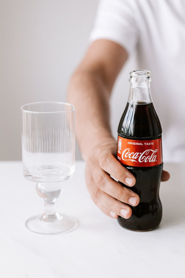 Crop Man Holding Bottle Of Coke At Table